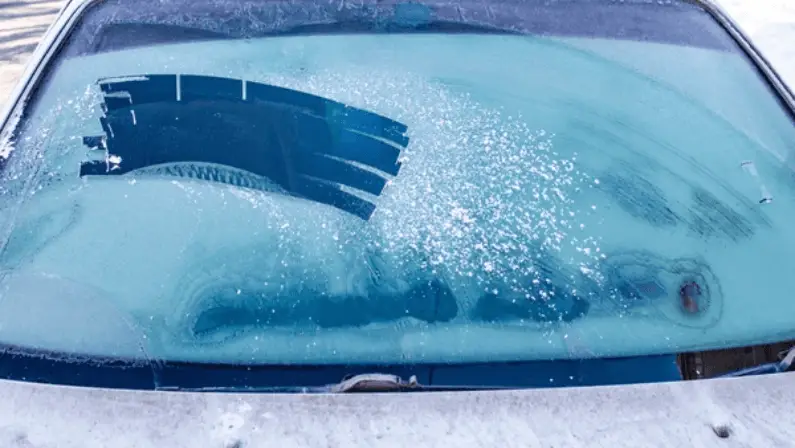 Frosted and ice-covered car windshield with wiper blades stuck under a thick layer of frost