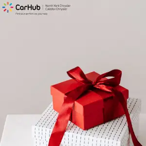Red ribbon-wrapped gift box on stacked white gift boxes, CarHub North York Chrysler Caledon Chrysler promotion