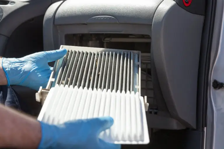 Technician in blue gloves installing new cabin air filter into vehicle glove box compartment