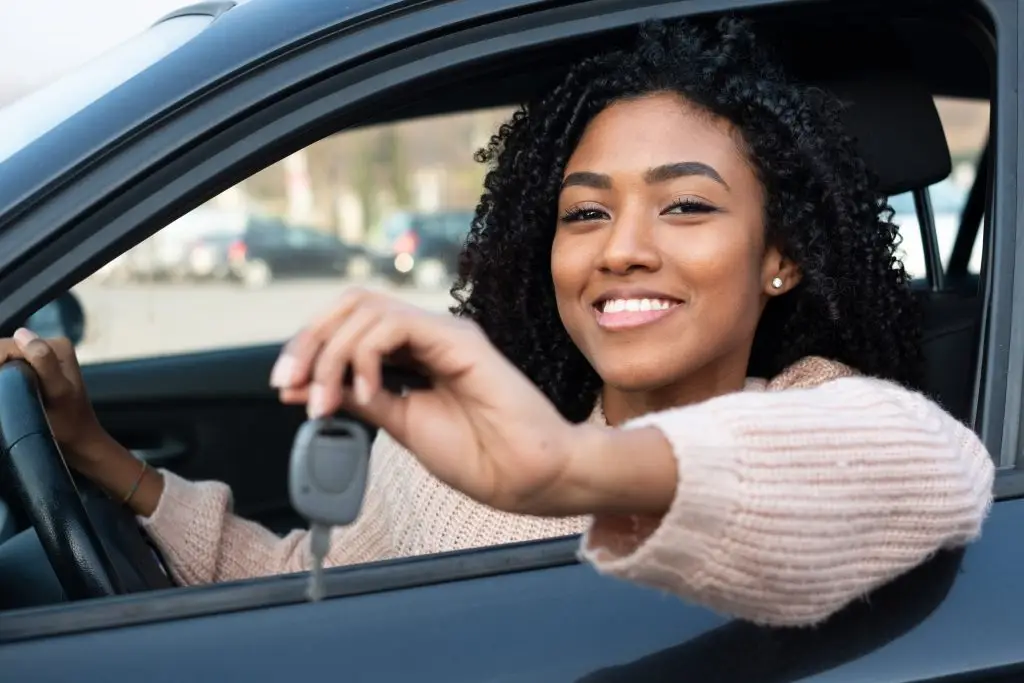 Smiling woman holding new car keys out the driver's side window