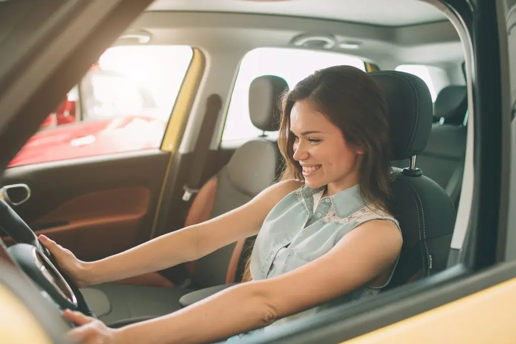 Closeup portrait happy, smiling, young attractive woman, buyer sitting in her new car isolated outside dealer, dealership lot office.
