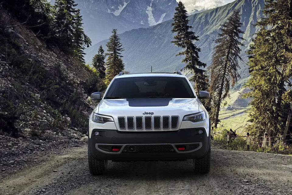 White Jeep Cherokee Trailhawk SUV front view on mountain gravel road