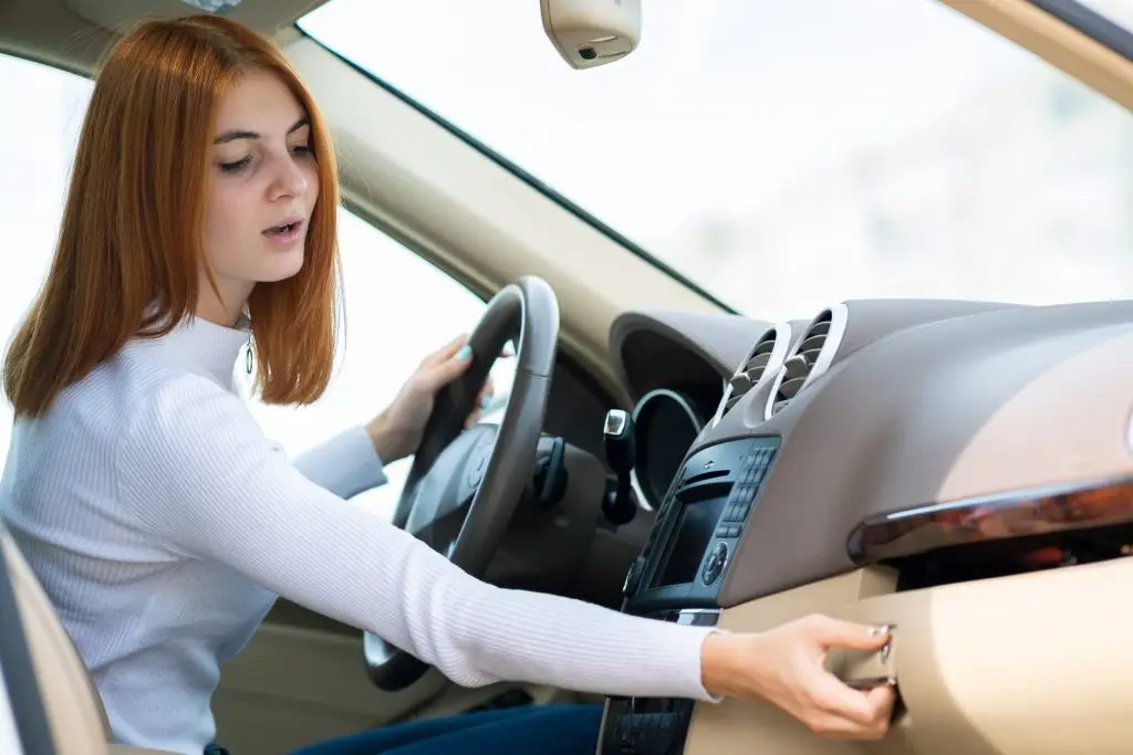 Woman sitting in driver's seat reaching into car glove compartment