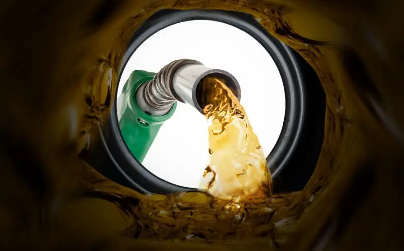 Close-up view inside car fuel tank of gas pump nozzle filling with amber fuel