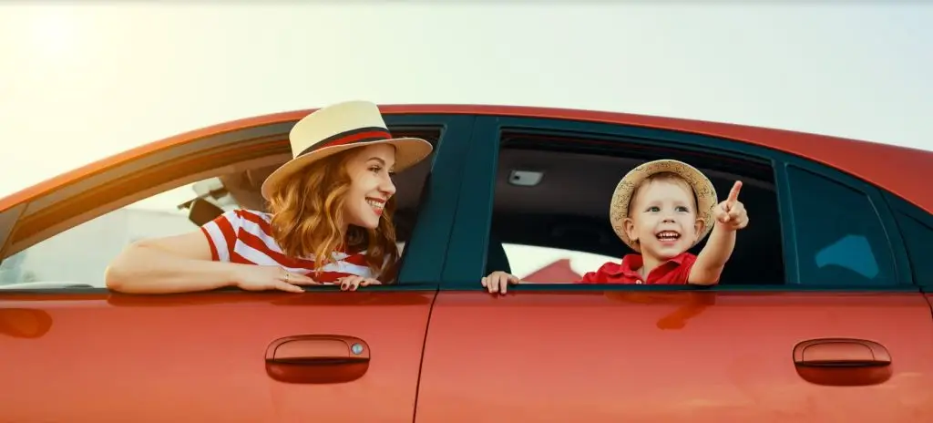 Happy mother and young son leaning out of red car windows wearing straw hats