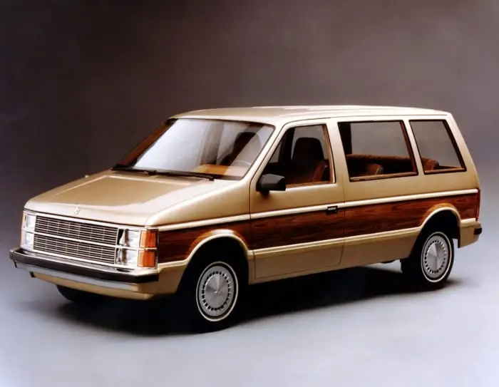 Vintage tan Dodge Caravan minivan with wood-panel siding, front three-quarter promotional photo