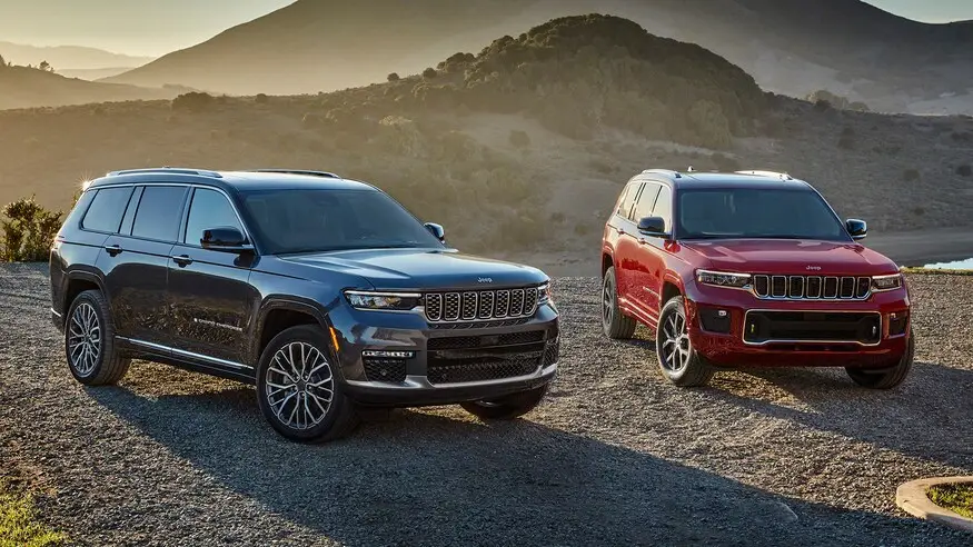 Black and red Jeep Grand Cherokee L SUVs parked on gravel at sunset with mountain backdrop