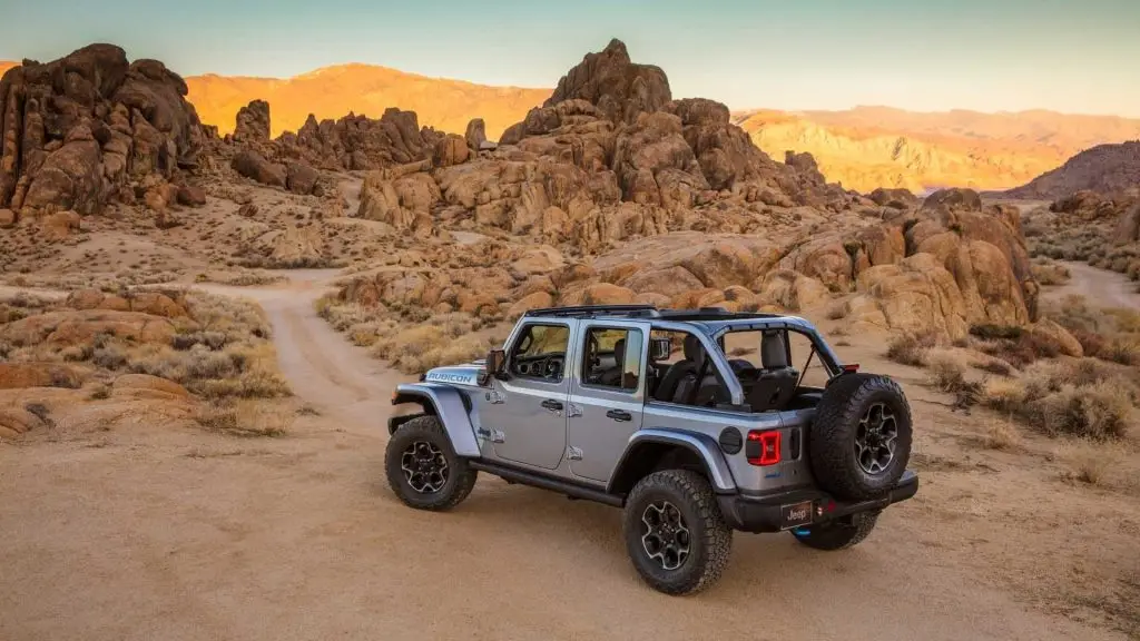 Silver Jeep Wrangler Rubicon Unlimited parked on desert trail among rock formations at sunset