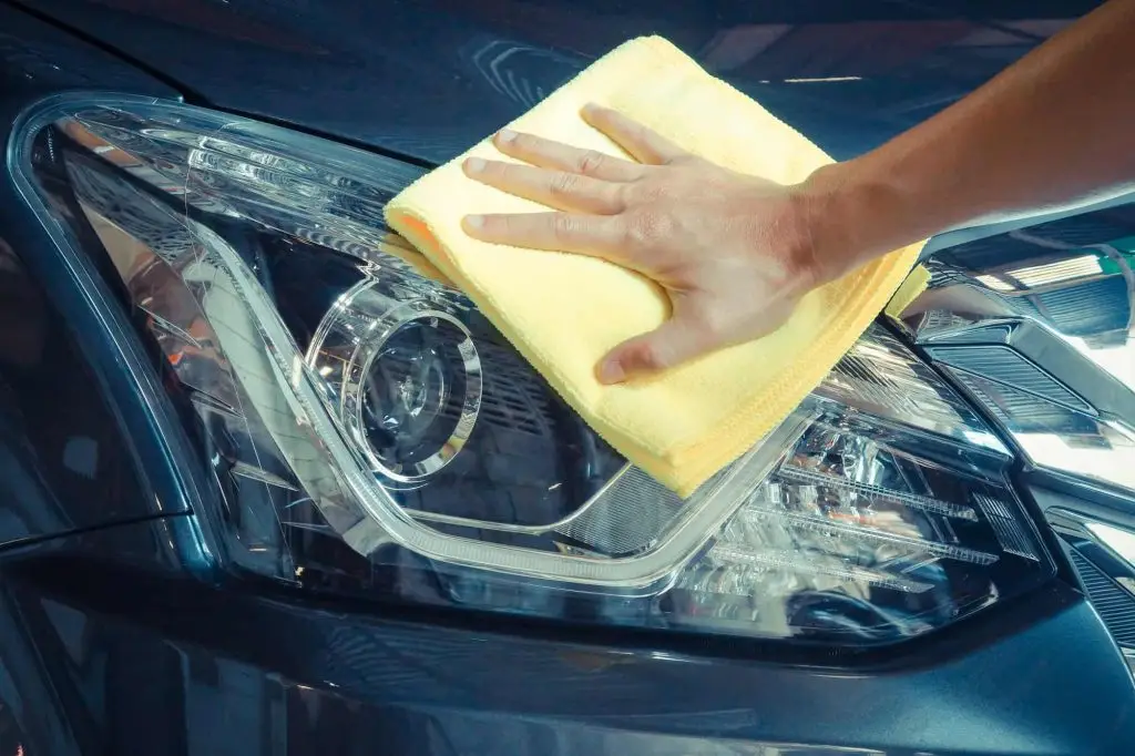 Hand cleaning car headlight lens with yellow microfiber cloth