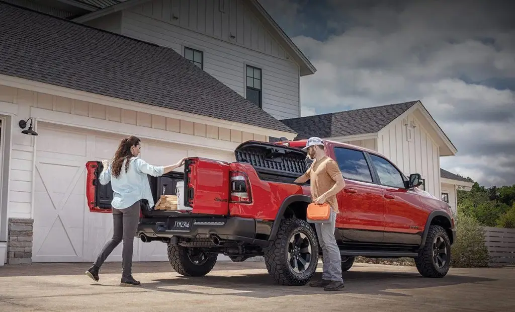 Couple loading cargo into red Ram 1500 TRX truck bed with RamBox storage at home driveway