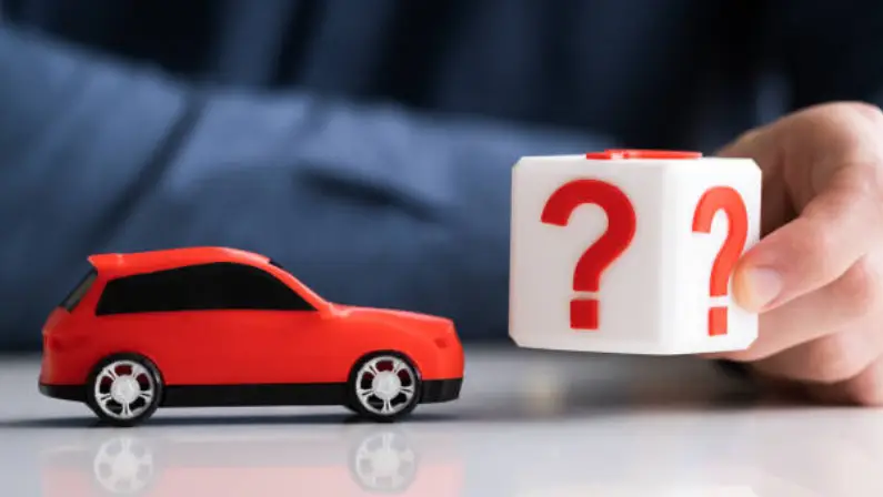 Red toy car next to a white question mark block held in a hand, symbolizing car buying uncertainty