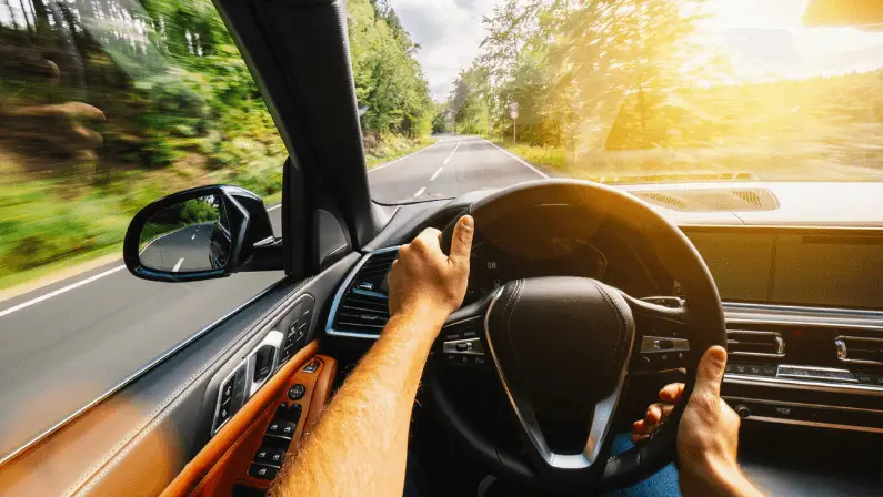 Driver's point-of-view shot of hands on the steering wheel while driving down a scenic tree-lined road