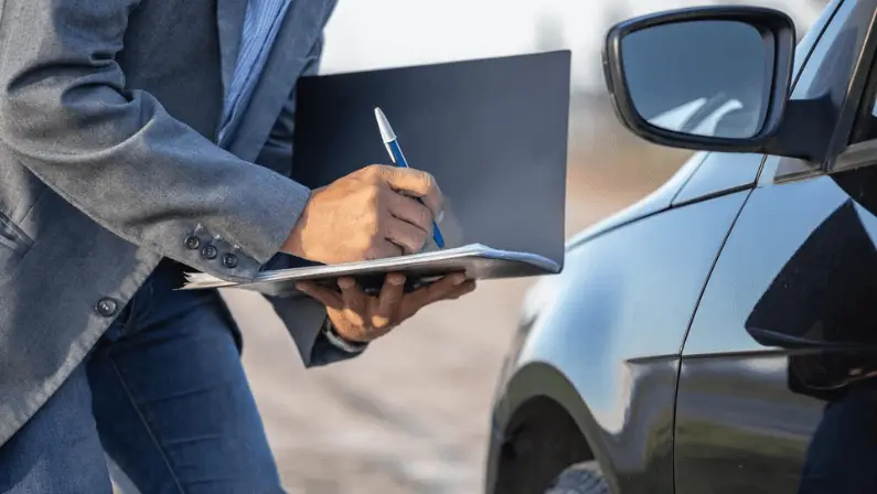 Person writing on a clipboard next to a black car, inspecting or documenting vehicle details