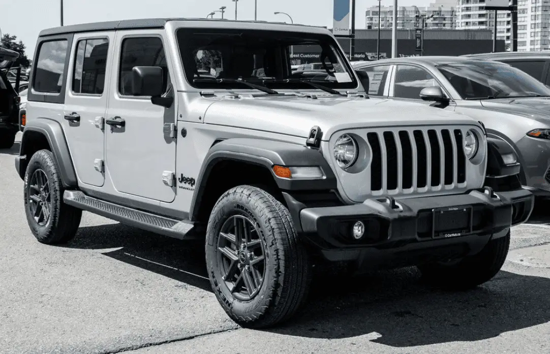 Silver Jeep Wrangler Unlimited parked in a dealership lot, black and white photo with red Jeep grille badge visible