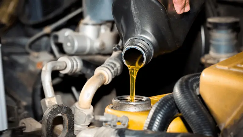 Close-up of golden motor oil being poured from a black bottle into a car engine's oil fill cap