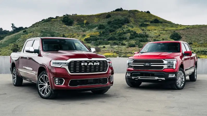 Red RAM and red Ford F-150 pickup trucks parked side by side with a grassy hill in the background