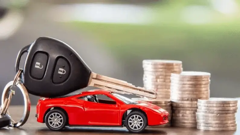 A car key fob resting on a toy red sports car model, next to stacks of coins, symbolizing car costs or value.