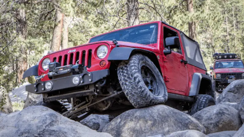 Red Jeep Wrangler crawling over large boulders on forest trail