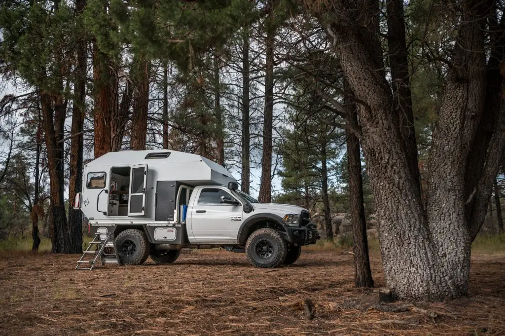 White Ram truck with off-road camper conversion parked in pine forest
