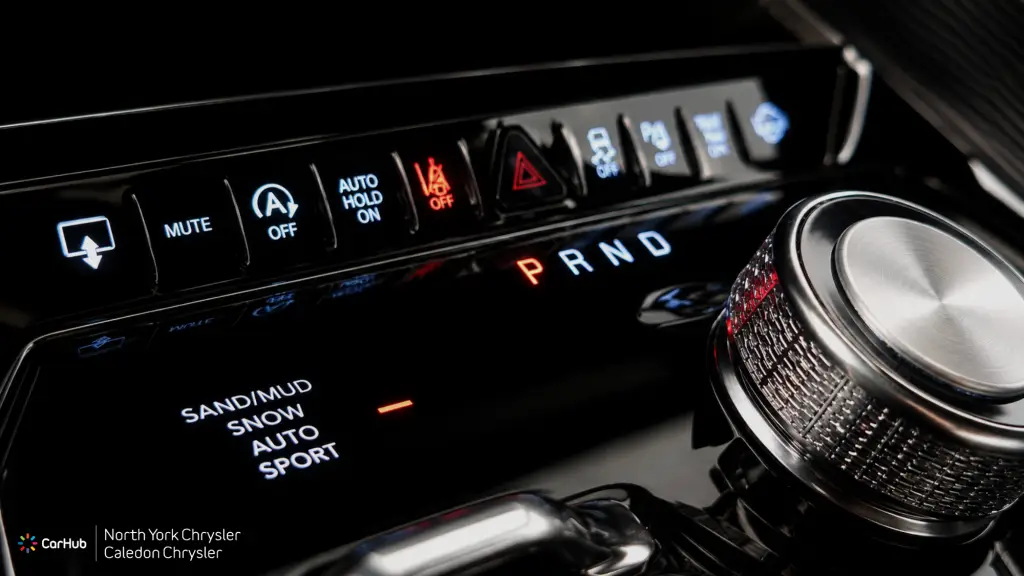 Close-up of the Jeep Grand Wagoneer center console controls, featuring the rotary dial gear shifter, Selec-Terrain traction management system, and back-lit buttons.